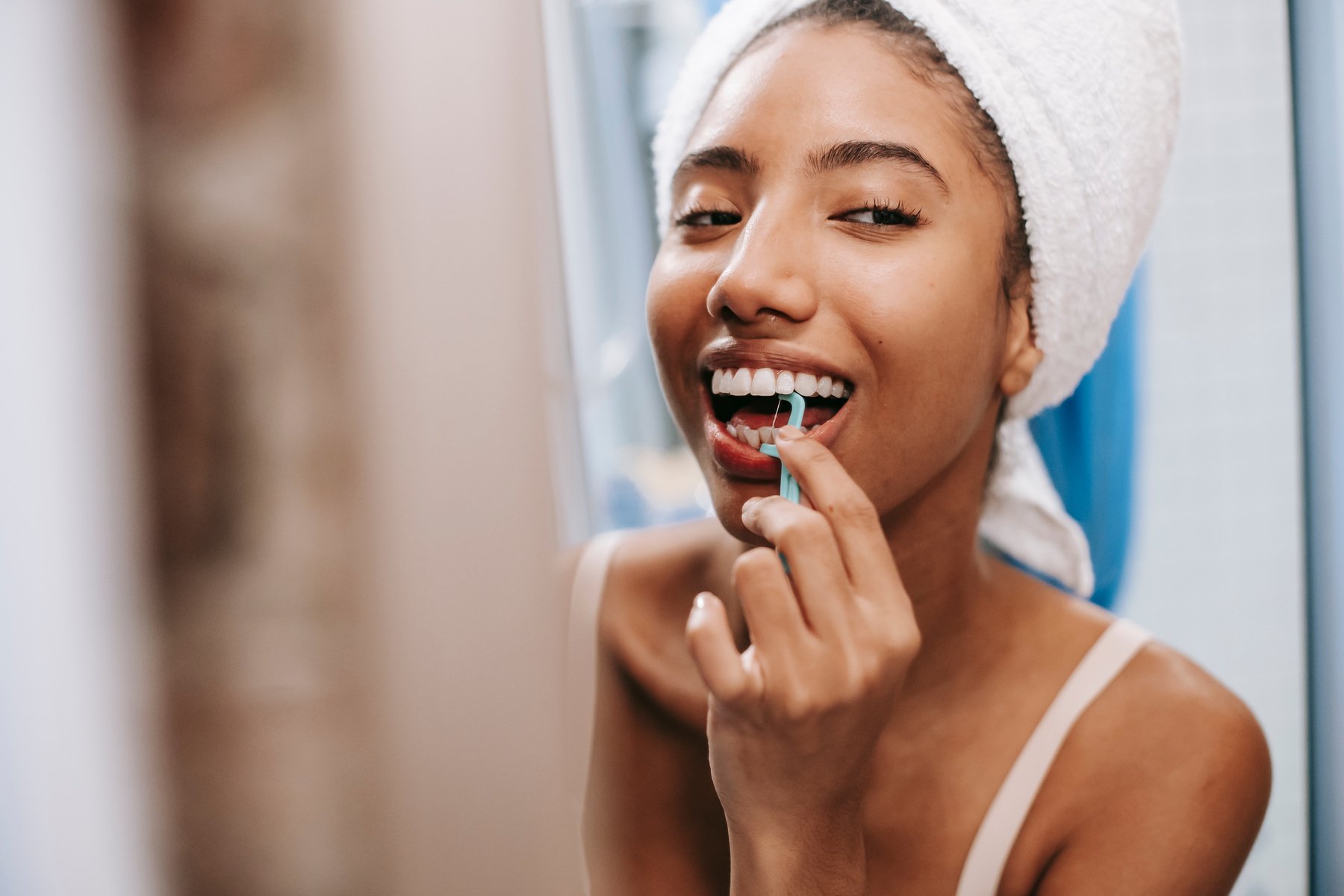 Cheerful woman cleaning teeth with flosser